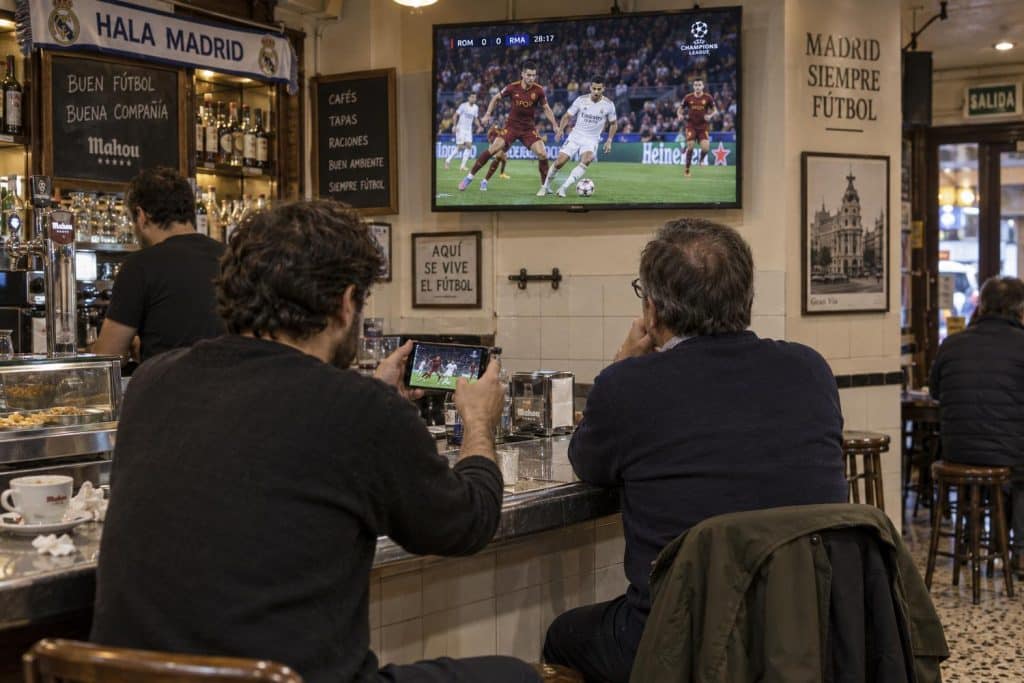 Escudos de la Roma y el Real Madrid ante una pantalla de televisión